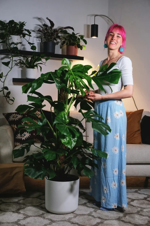 a woman in a long dress holds onto her houseplant