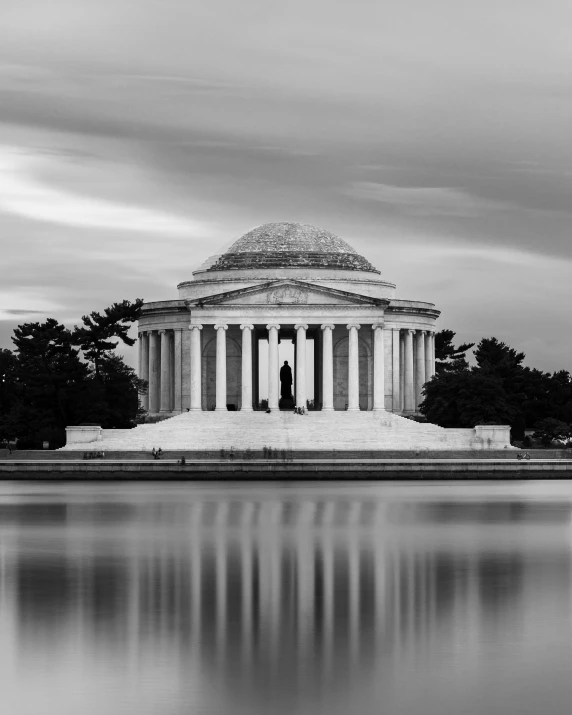 the jefferson memorial is reflecting in water as it sits in the middle of a large park