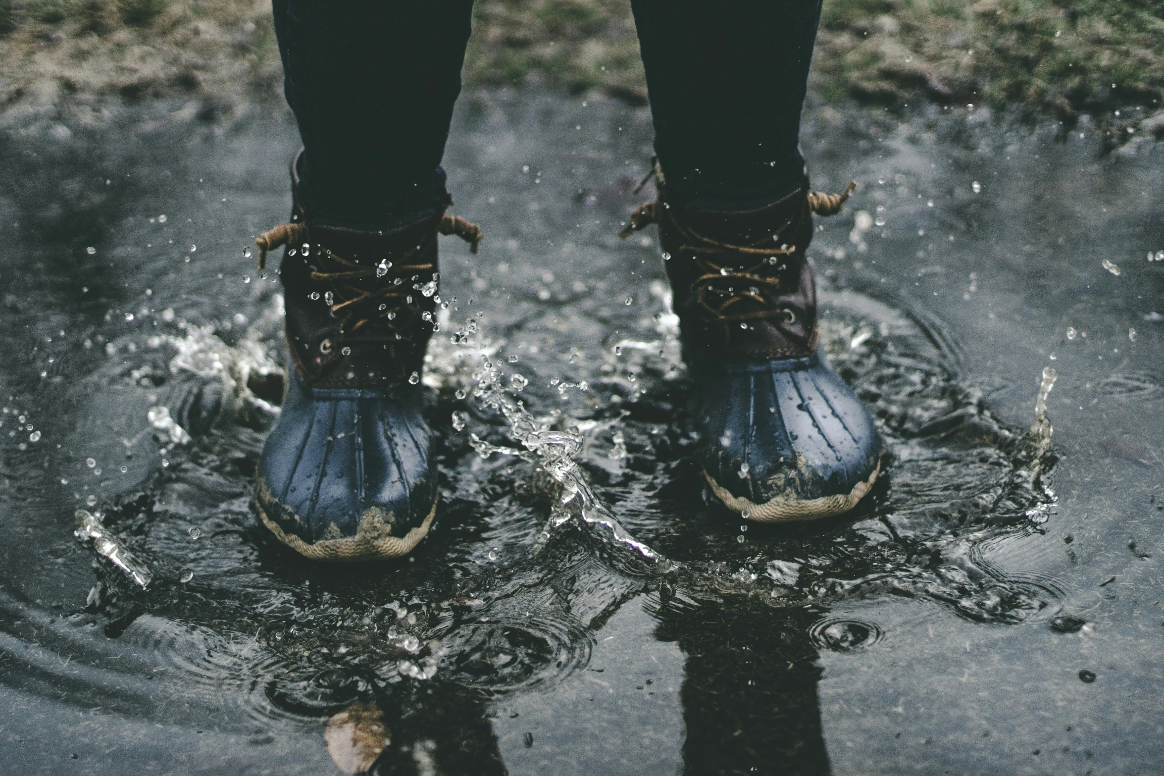 a pair of feet in water boots next to a tree