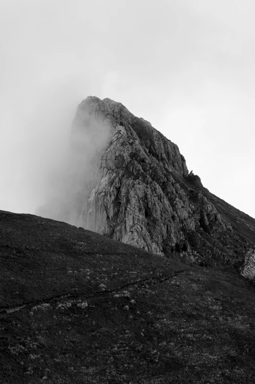 a rocky mountain in the fog near a grassy field