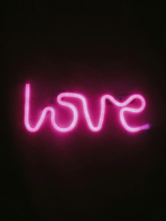 a pink neon sign in the dark that reads love