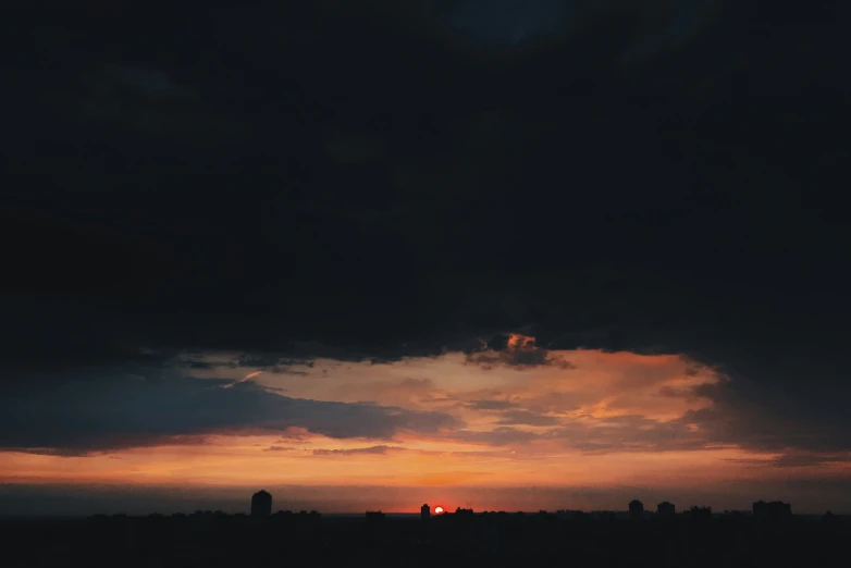 dark clouds cover the sun set over city skylines