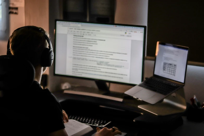 two computer screens are behind a man's headphones