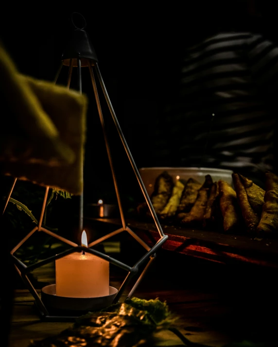 a lit candle sits in an iron lantern next to some bread