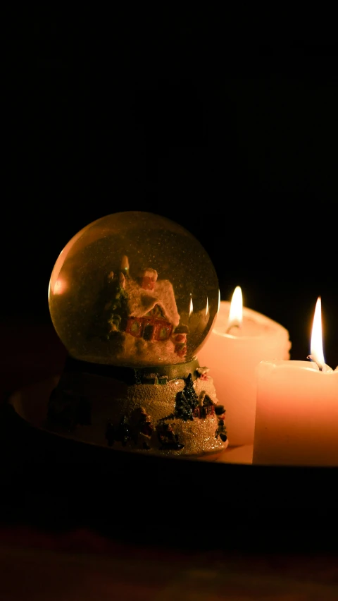 two white candles are next to some snow globes