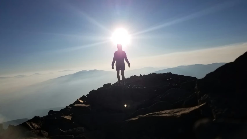 man on top of a mountain with sun peeking down