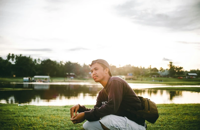 a man sitting in front of a lake wearing white pants