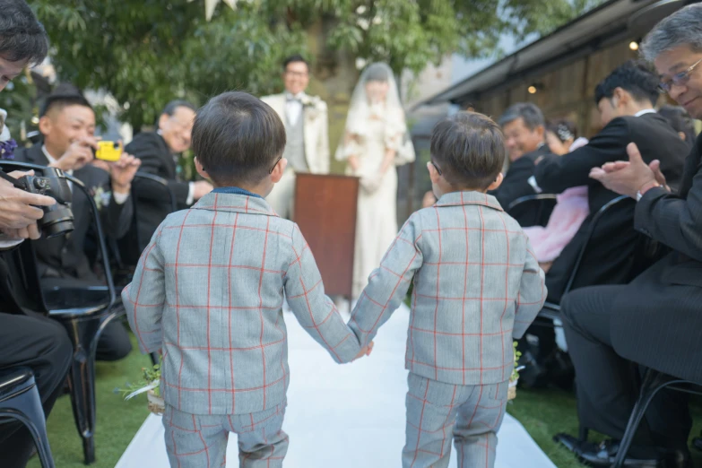 two children in suits walking down a walkway during a wedding