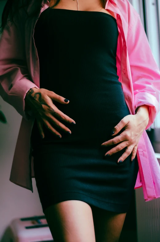 a pregnant woman in her black dress has her hands on her hips