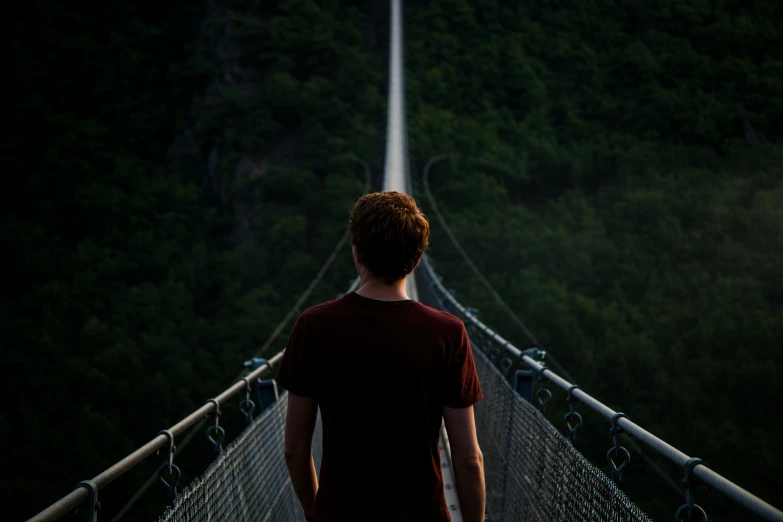 a man walks across a suspension bridge, towards mountains