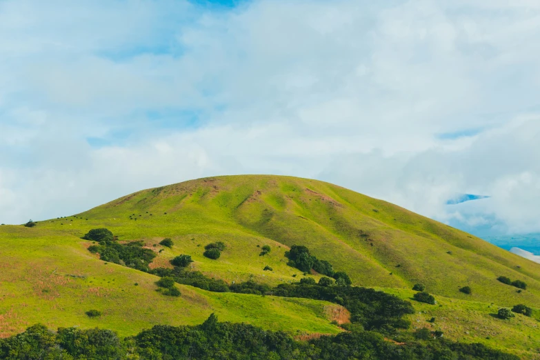 a green hills covered with trees and clouds