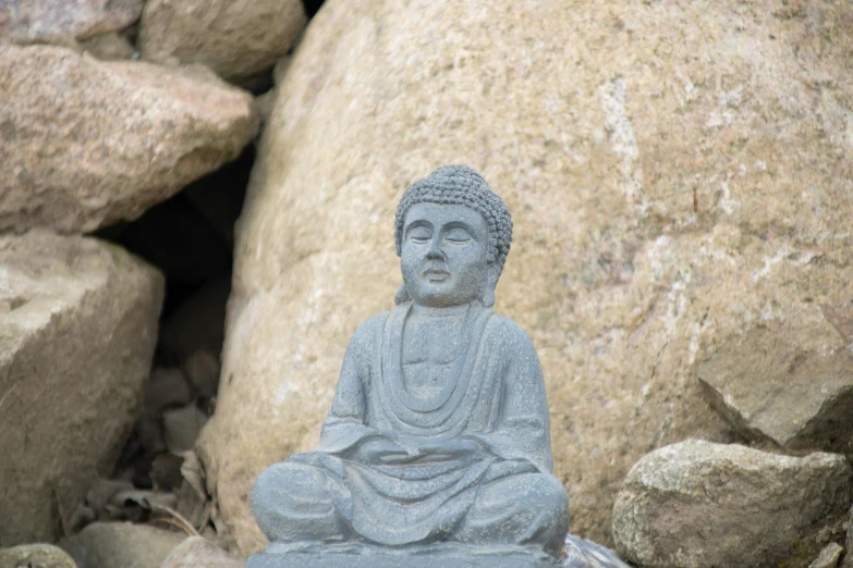 the buddha statue is sitting beside some large rocks