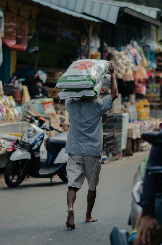 a man walking in the street carrying an open bag on his head