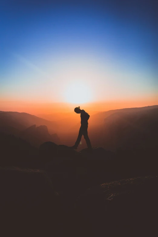 silhouette of man carrying backpack with sun setting in background