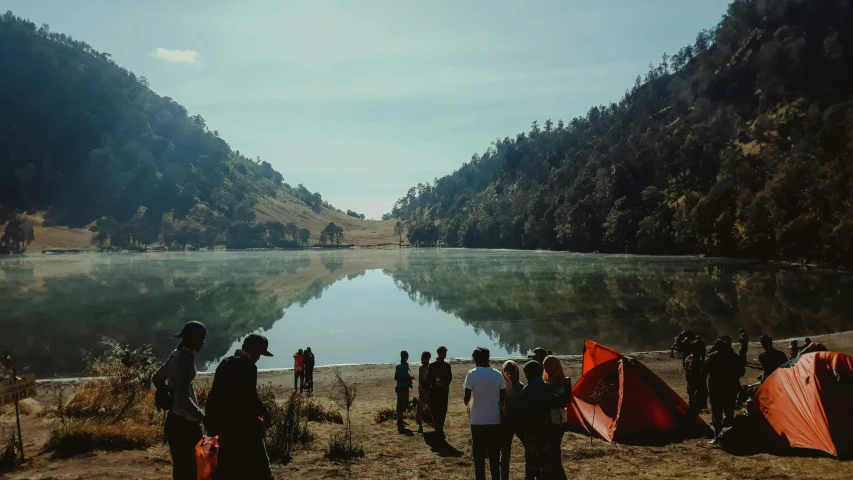 some people are standing near some tents on a hill by the water