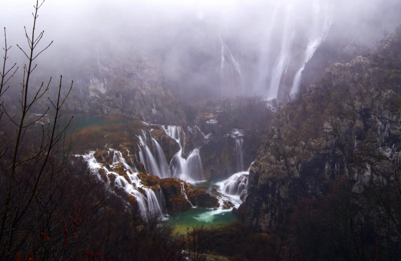 a large waterfall in a green pond surrounded by trees