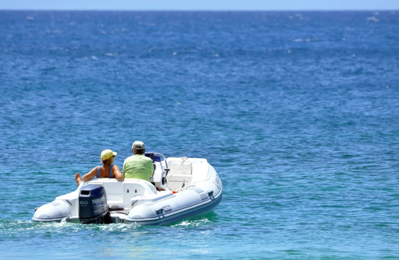 two people sitting on a white motorboat in the blue water