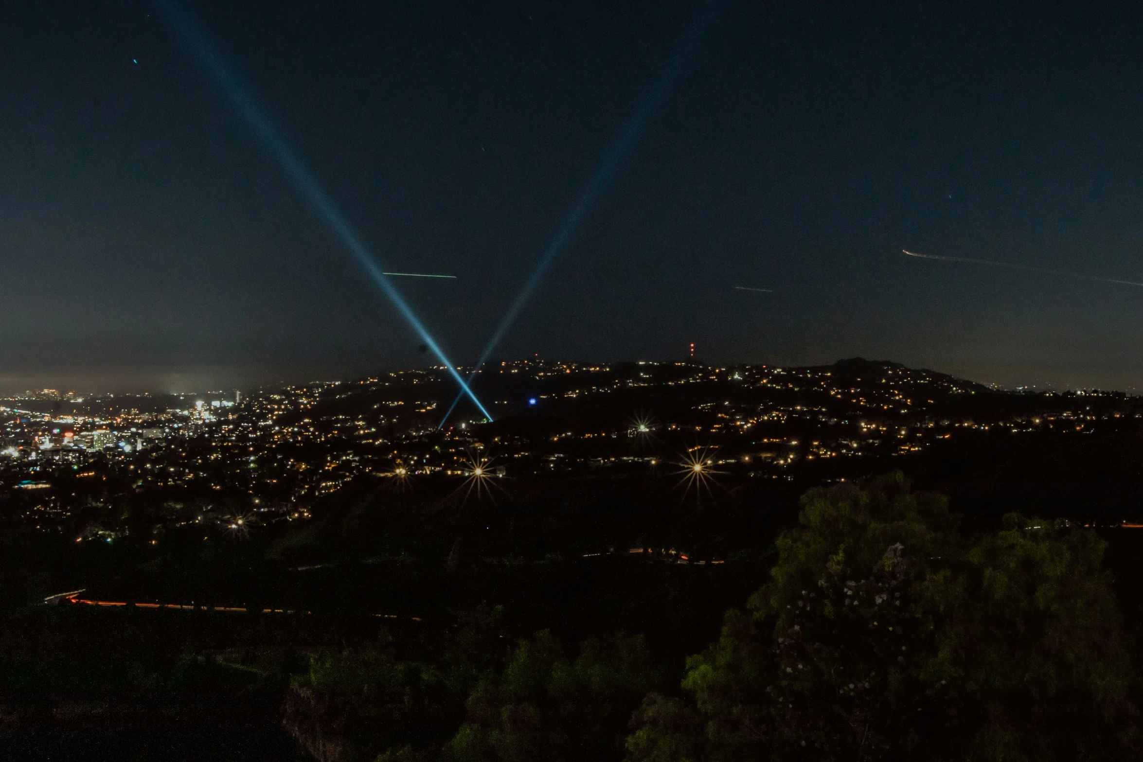 a view of the city at night with beams of light and blue haze