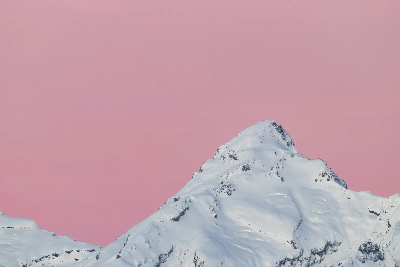 a snowy mountain is against a pale pink sky