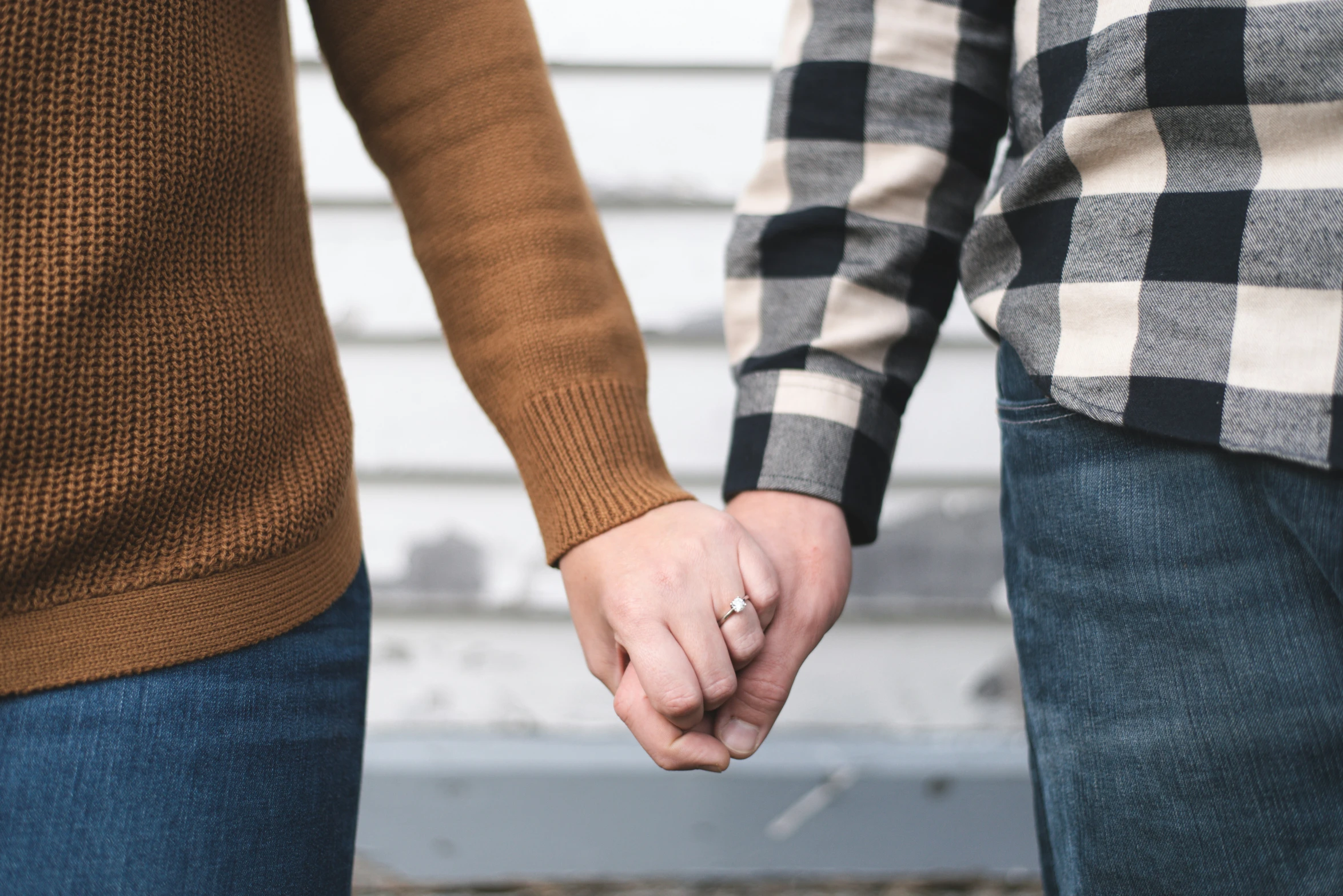 a couple holding hands, while standing against a wall