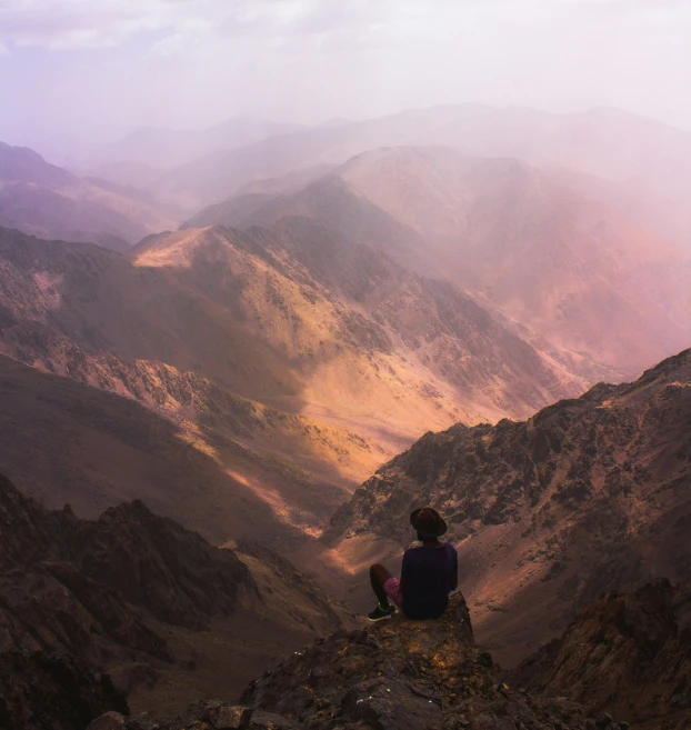 person sitting on cliff looking out on mountain view