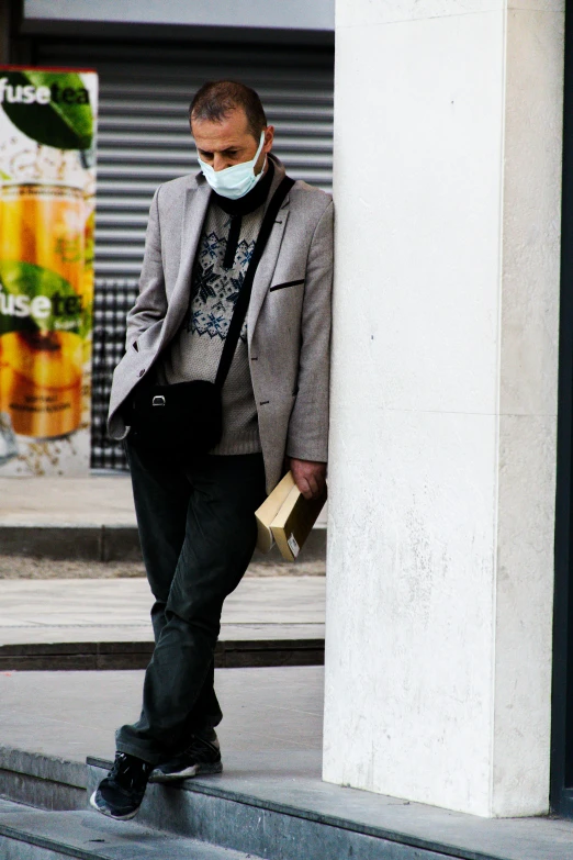 man leaning on column in city wearing mask with purse