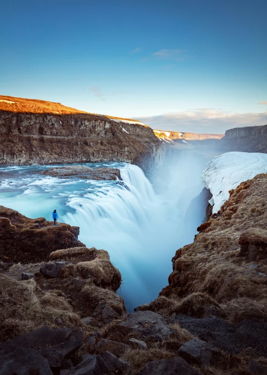 an icy river with a person standing on the rocks near it