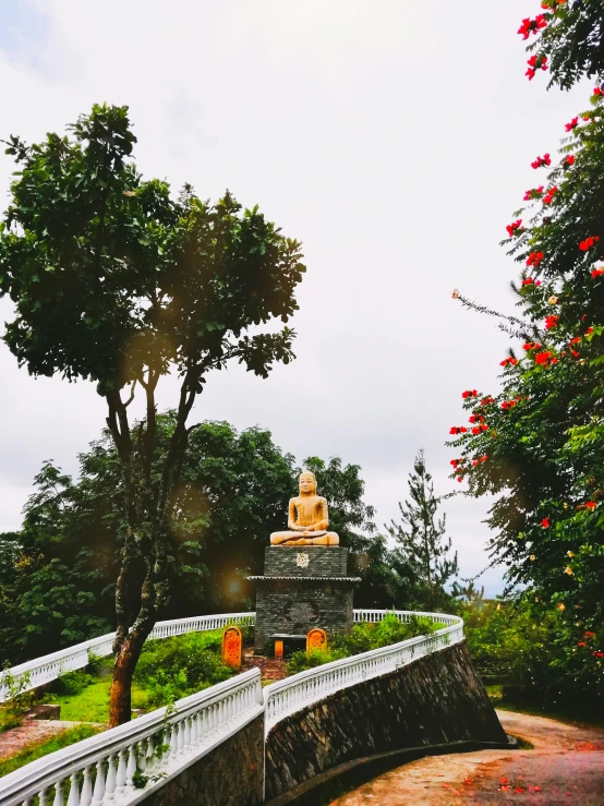 a pathway lined with trees and flowers leading to a statue