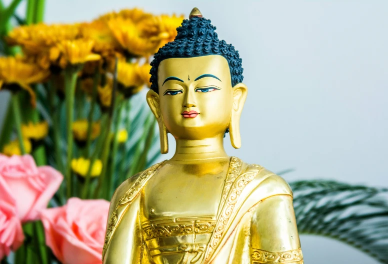 a statue of buddha sitting next to some flowers