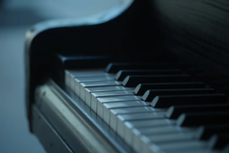 a piano with an angled keyboard sits in the shadows