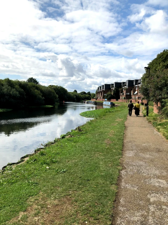 two people walking on the grass near the water