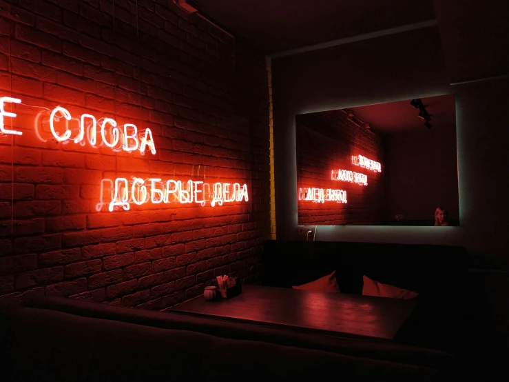 a brick wall with red neon sign with a mirror in the back