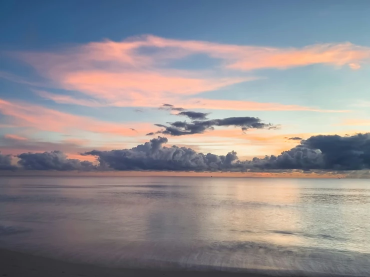 a sunrise view from the beach with clouds above