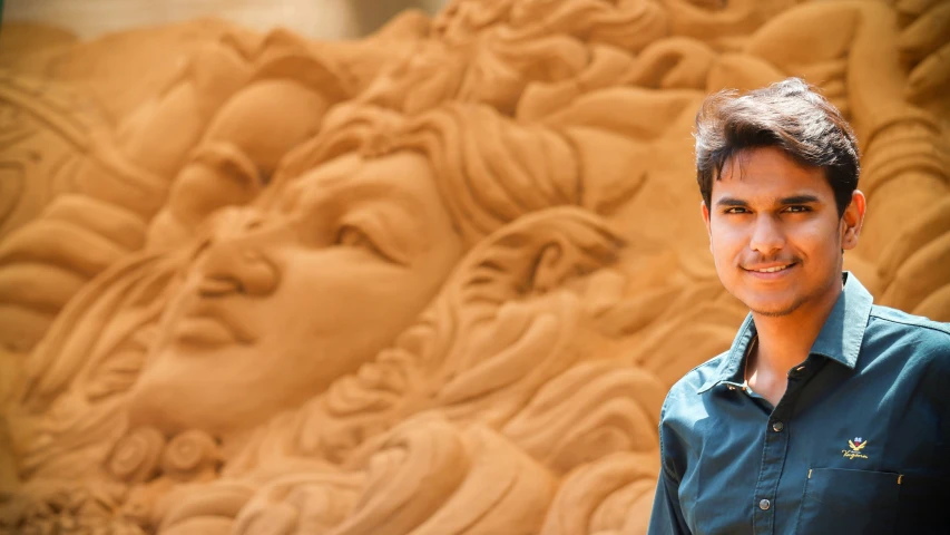 a guy posing in front of a wall sculpture