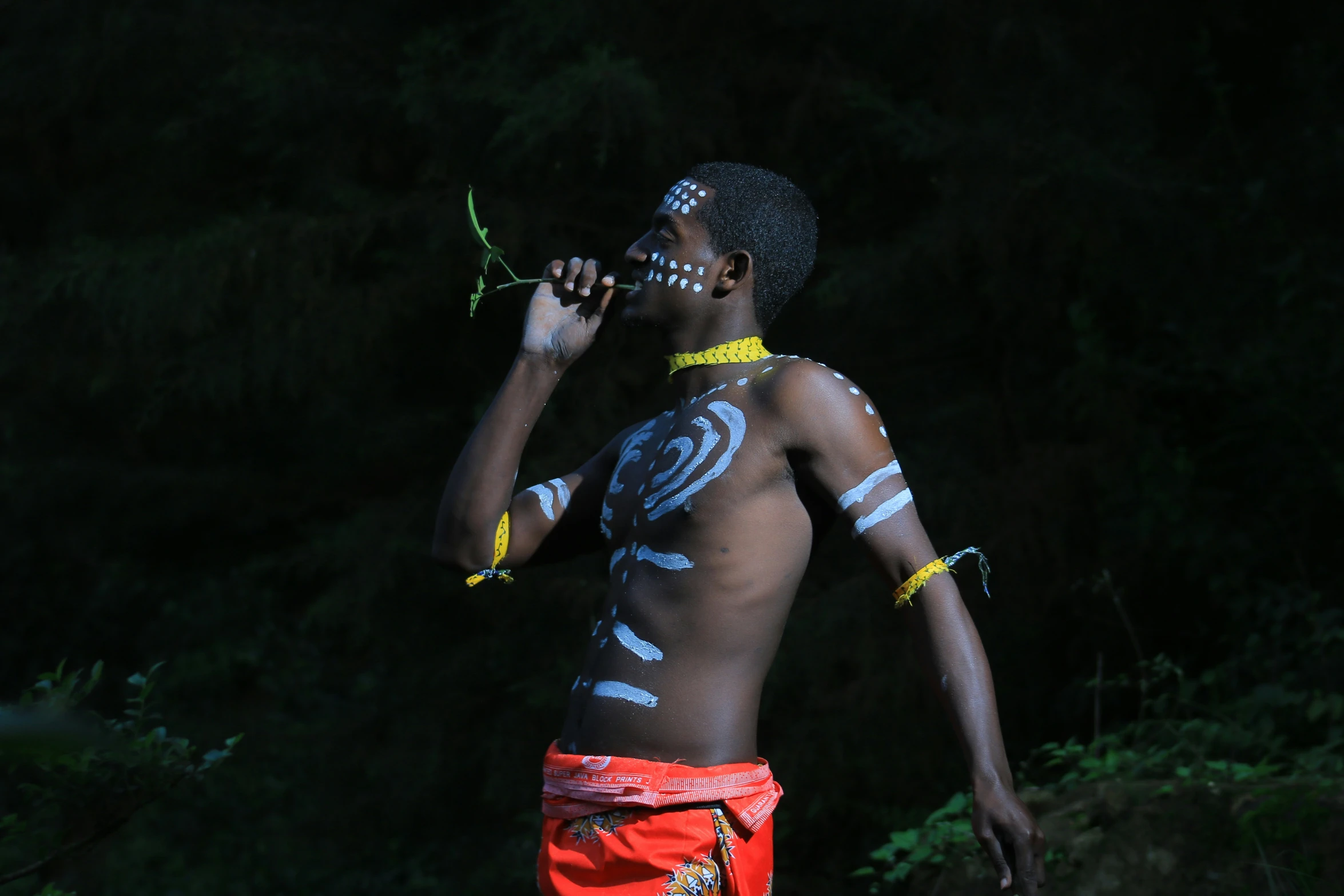 a man with white makeup and bright blue patterns on his face drinking from a water bottle