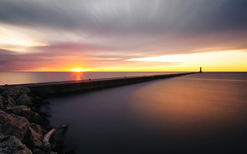 the sunset is setting on a very long pier