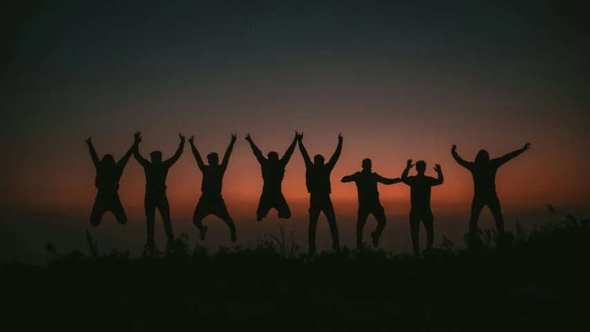 silhouettes of people with arms and legs raised, at sunset