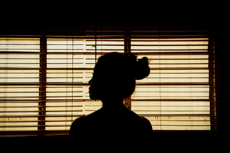 a person standing by a window with blinds closed