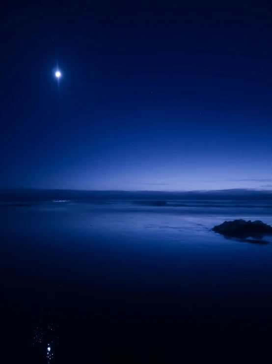 the moon over a calm blue lake on the dark night