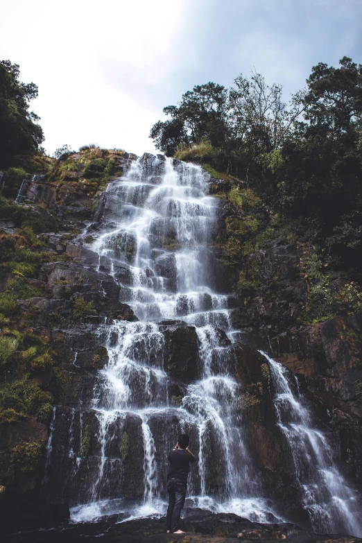 man standing in front of huge waterfall with trees around