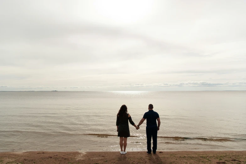 a couple holding hands while standing near the ocean
