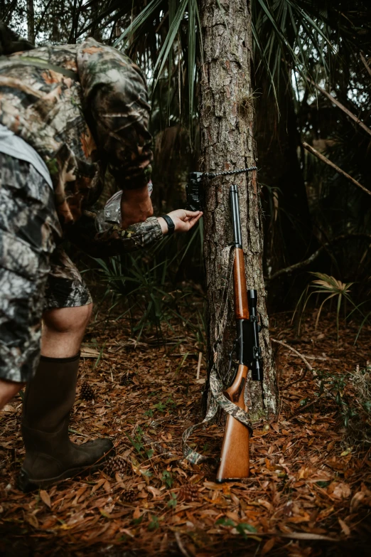 a man in camo crouching next to a tree with his gun and rifle