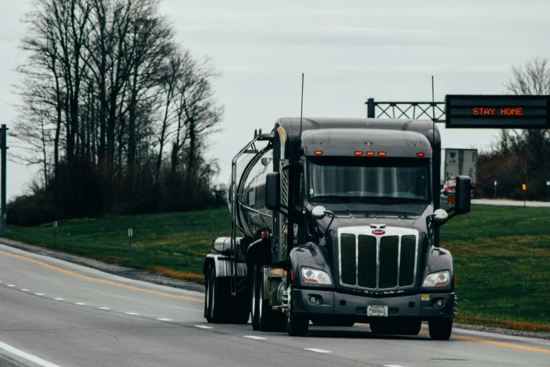 semi truck driving down road with trees and a sky in background