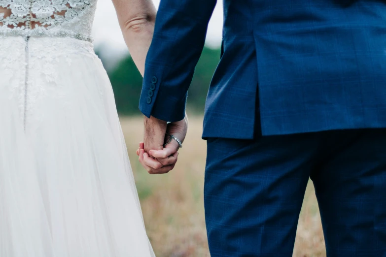a bride and groom holding hands in a field