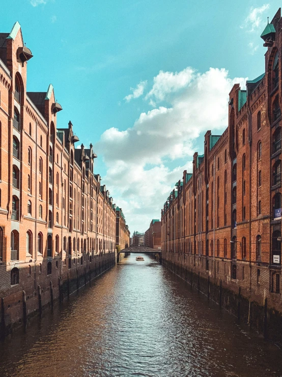 a river runs past a row of old buildings along a street lined with red brick