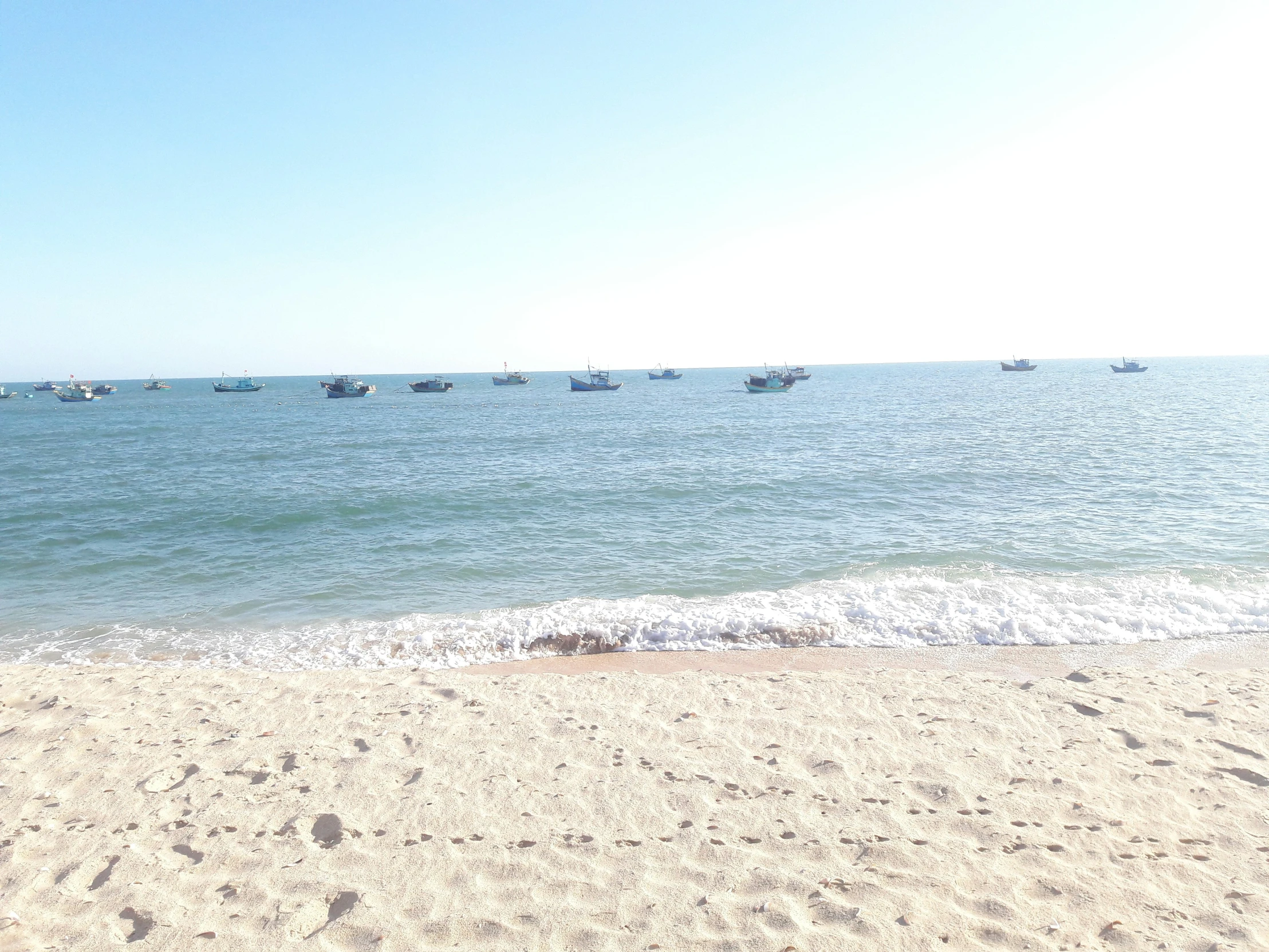 a group of boats floating in the water near a beach