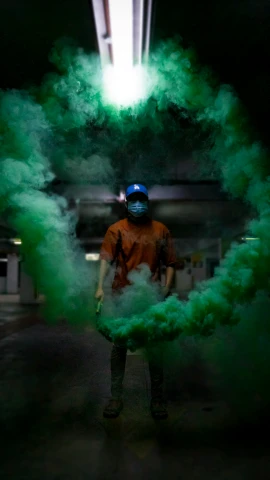 man with goggles wearing orange is covered in green smoke
