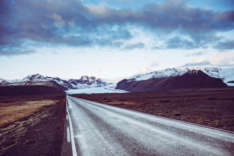 an empty road with snowy mountains in the background