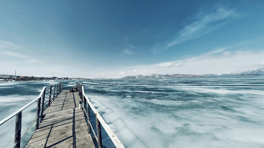 a wooden dock stretching into the water near snow covered mountains