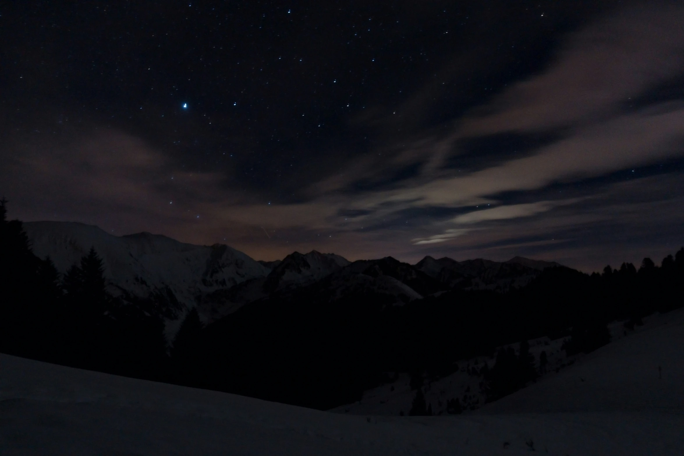 the night sky with clouds and stars above some mountains